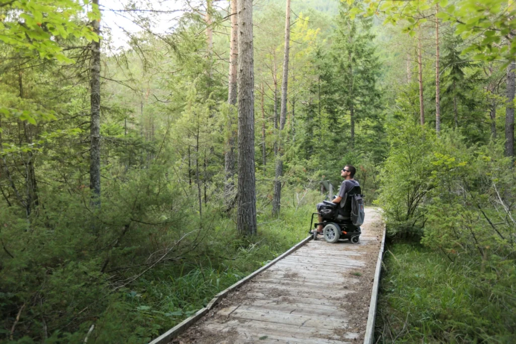 Mężczyzna na wózku elektrycznym poruszający się po drewnianej trasie w lesie, Zakopane dla osób z niepełnosprawnościami i wybór dostępnego noclegu blisko natury